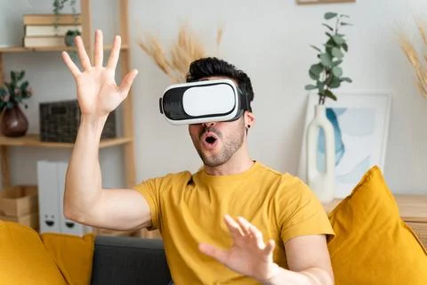 Man sitting on sofa wearing virtual reality goggles. Stock Photos