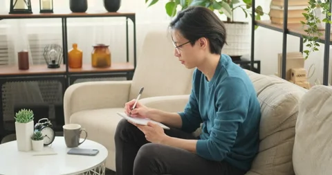 Man sitting on sofa writing in notepad Video stock 145292902