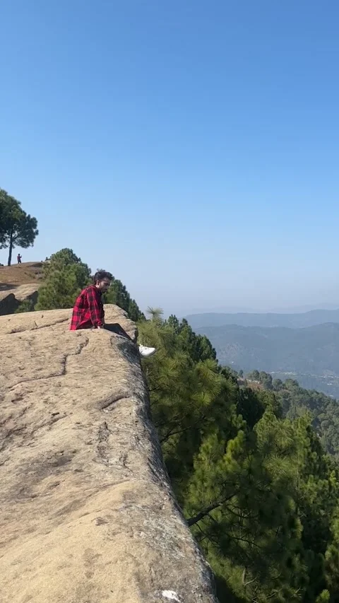 Man Sitting on Steep Rocky Cliff Edge Overlooking Vast Mountain Valley at Sunset Stock Footage 330135829