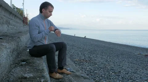 A man sitting on the steps near the pebble beach of the ocean. It scans messages Stock Footage 67620848