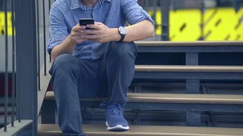 Man sitting on the steps of the stairs and talking on the phone Stock Footage 143472238