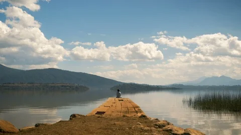 Man sitting still at the edge of a dock taking in the view Stock Footage 89213394