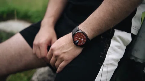The man is sitting on a stone, and he has a watch on his wrist Stock Footage 344899069