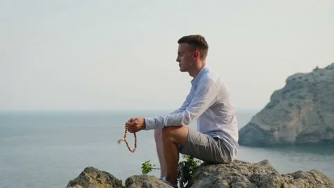 Man sitting on a stone cliff overlooking the sea and meditating Video stock 159594828