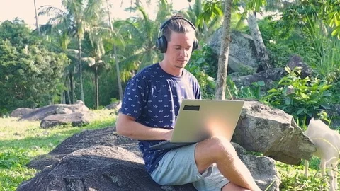 A man is sitting on the stone while working as a freelancer. Video stock 122498526