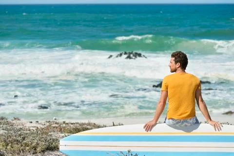 Man sitting on a surfboard on the beach Stock Photos