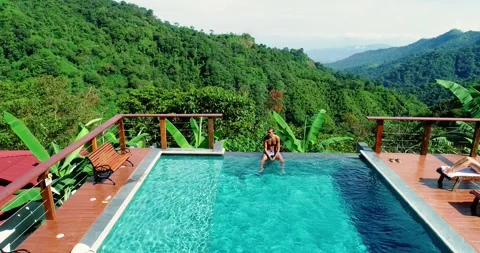 Man sitting on swimming pool's deck as his girlfriend tans on chaise lounge. Stock-Footage 278793597