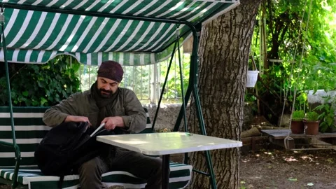 Man sitting on swing takes laptop out of his bag and works Stock Footage 145265953