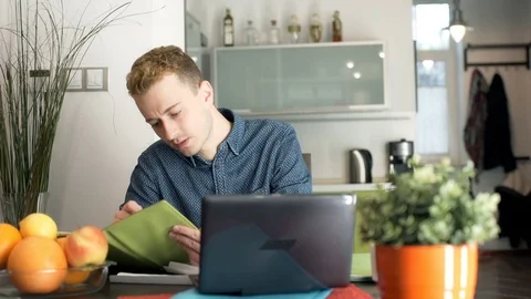Man sitting by the table and doing notes while checking checks Stock Footage 70379938
