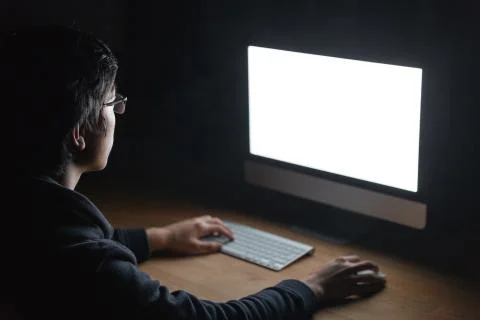 Man sitting at table and using computer in dark room 스톡 사진