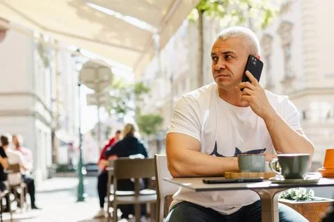 A man is sitting at a table in a cafe, talking on his cell phone Stock Photos