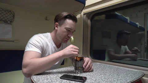 Man is sitting at a table in a compartment of a moving train, drinking tea Stock Footage 264021289
