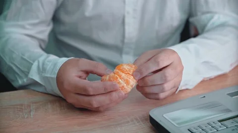 The man sitting at the table is eating a tangerine. Food in the workplace. Stock Footage 146264355