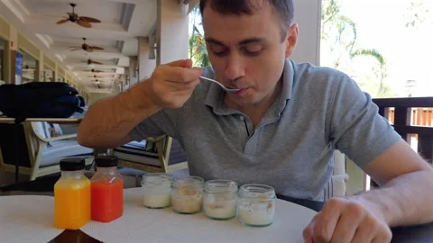 A man is sitting at a table eating yogurt with a spoon Stock Footage 264733614