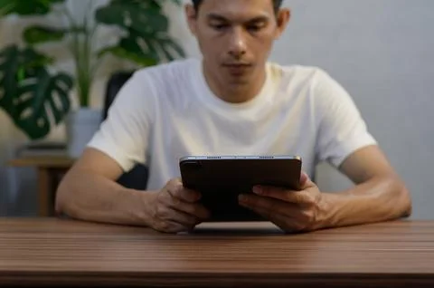 Man Sitting at Table Engaged with Tablet Amidst Indoor Plants Stock Photos