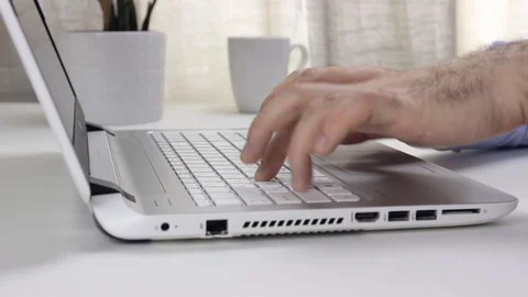 Man sitting at a table in front of a laptop and is typing on the keyboard Stock Footage 128103831