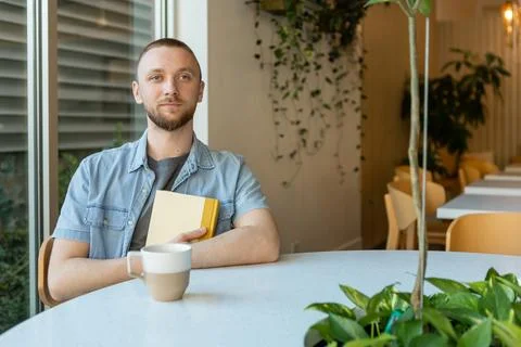 Man sitting at a table holding a notebook and a cup in a bright space for o.. 写真素材