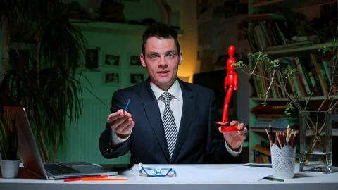 A man sitting at a table holds a model of a man’s figure in his hands. Stock Footage 128026857