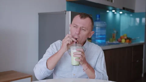 Man sitting at a table at home, drinking a milkshake from a cup through a straw. Stock Footage 332206160
