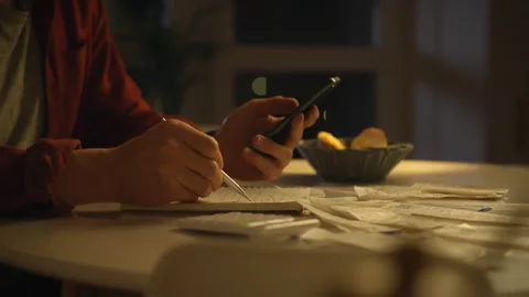 A man sitting at a table in the kitchen painstakingly calculates expenses in Stock Footage 323724140