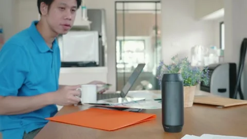 A man is sitting at a table with a laptop and a smart speaker Stock Footage 314455614
