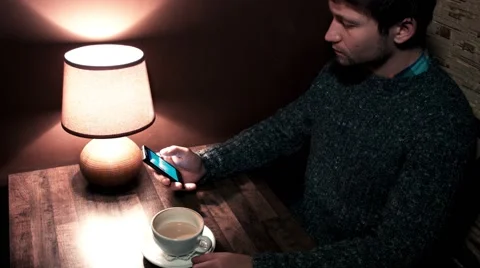Man sitting at the table playing on phone and drinking coffee Video stock 56250978