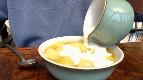 Man sitting at a table pouring cream onto pineapple pieces. Stock Footage 89960195