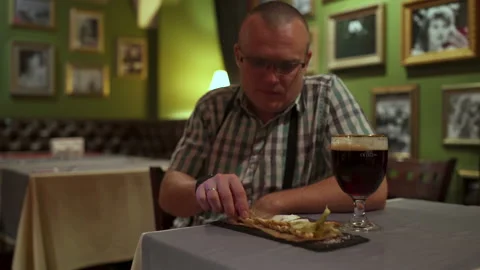 The man is sitting at a table in the restaurant drinking a beer with crackers Stock Footage 91314973
