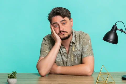 Man sitting at table supporting head with hand staring blankly, feeling Stock Photos