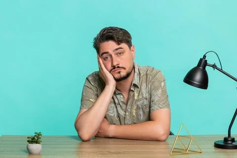 Man sitting at table supporting head with hand staring blankly, feeling Stock Photos