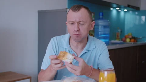 A man sitting at a table , takes a product out of its packaging and tastes it Stock-Footage 332201802