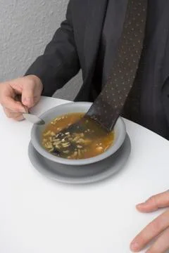 Man sitting at table with tie floating in bowl of soup Foto stock