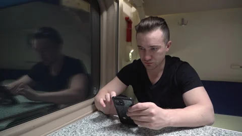 Man is sitting at a table on the train, talking via video link using his phone Video stock 264585409