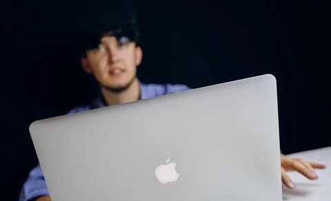 A man is sitting at a table using an Apple laptop computer for his work 스톡 사진