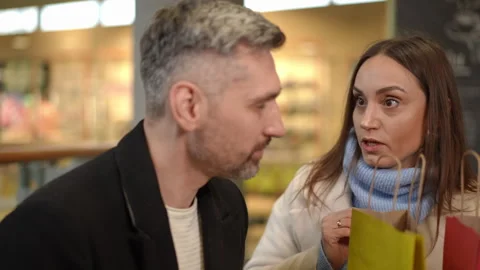 Man Sitting at Table While Woman Arrives with Shopping Bags During Sale Season Vidéo 296772325