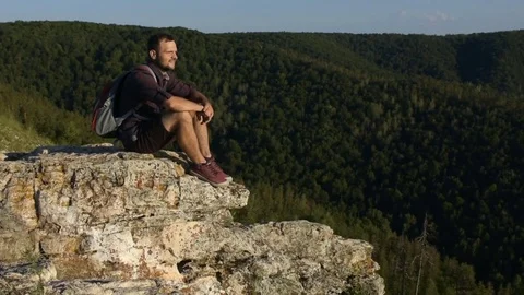Man sitting on top of a cliff and looking into the camera and smiling. Stock Footage 72597366