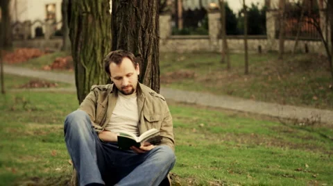Man sitting by the tree and reading book, dolly shot Stock Footage
