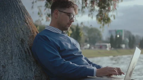 Man Sitting by Tree in the Park Typing on Laptop Stock Footage 237057965