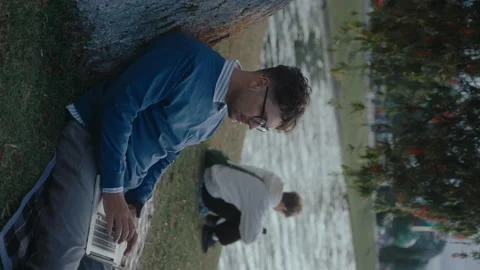 Man Sitting by Tree Working on Laptop in the Park Stock Footage 237058109