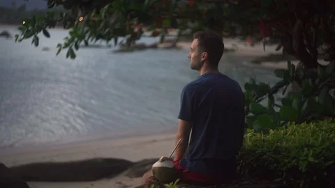 Man sitting on the tropical beach, drinking coconut and opens his hands wide. Stock Footage 122436004