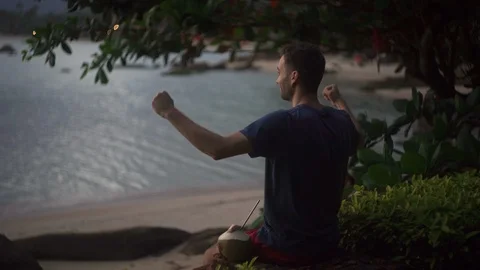 Man sitting on the tropical beach, drinking coconut and express Stock Footage 122437560