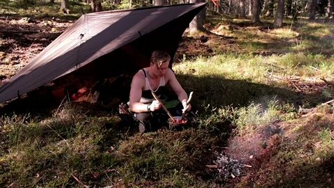 Man sitting under a tarp by a fire, eating Stock Footage 91649325