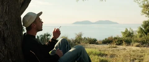 Man sitting under a tree and smoking a cigarette sea view at sunset Stock Footage 324920091