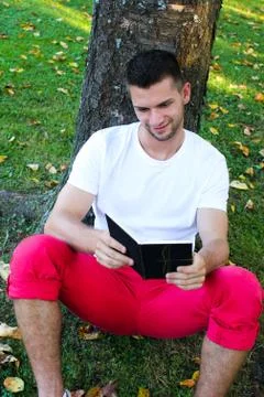 Man sitting under a tree reading a book Stock Photos