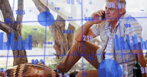 Man sitting up under trees taking call viewing travel metrics, blue data overlay Stock Footage 331227274