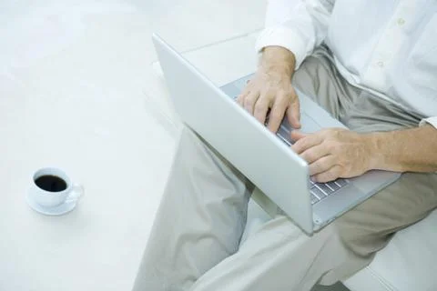 Man sitting using laptop computer, cup of coffee beside him, cropped view Stock Photos