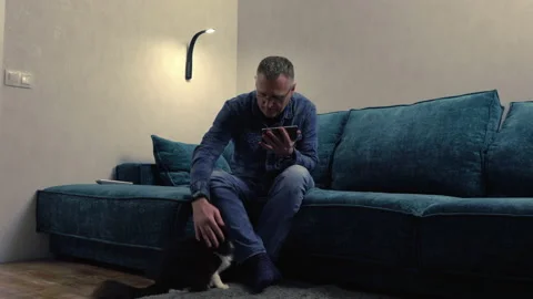 Man sitting using a mobile phone with cat at his feet Stock Footage 158931572