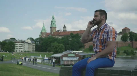 Man sitting on wall and talking by smartphone. Vídeo Stock 52695888