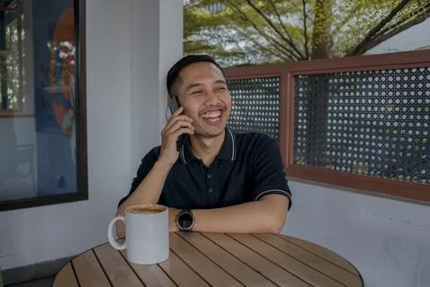 Man Sitting While On A Phone Call, Laughing And Looking To The Side, Enjoyi.. Stock Photos