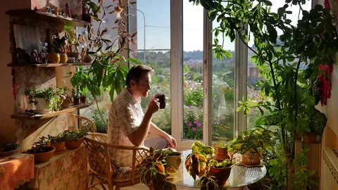 Man Sitting on a Wicker Chair Drinks Coffee Looking Through Open Window of Stock Footage 71632117